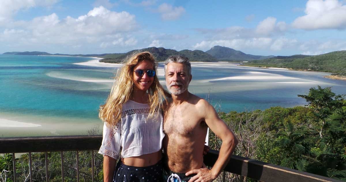 Tomas australia chica y señor posando sonriendo para cámara y detrás el agua cristalina del mar